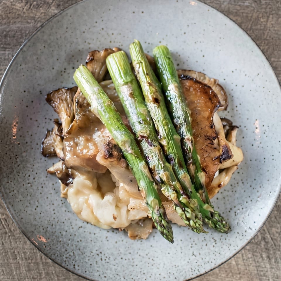Grilled asparagus spears atop sautéed mushrooms and creamy polenta on a speckled grey plate.