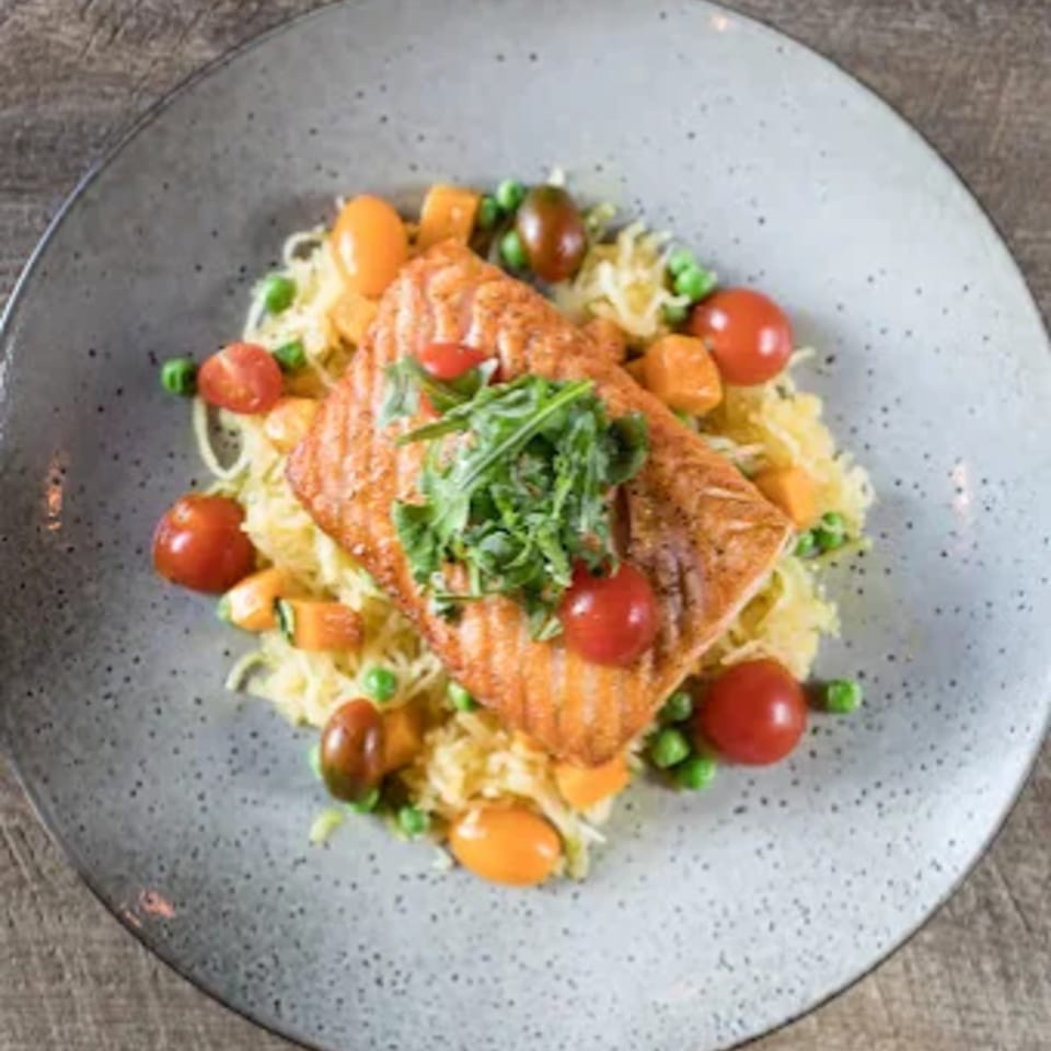Grilled salmon fillet with arugula, cherry tomatoes, peas, and butternut squash over spaghetti squash.
